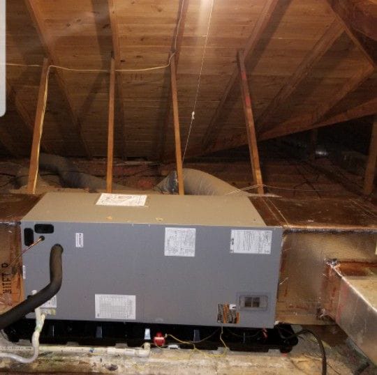 HVAC unit installed in an attic, with exposed wooden beams above and ductwork extending out of view, emphasizing home heating and cooling systems.