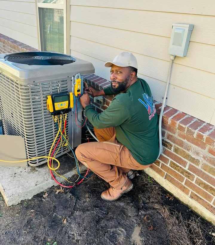 Herman Williams smiles while installing an HVAC system, wearing a cap and green long-sleeve shirt with the company logo, Wms Heating & Air Conditioning, AC Repair in Monroe, LA.
