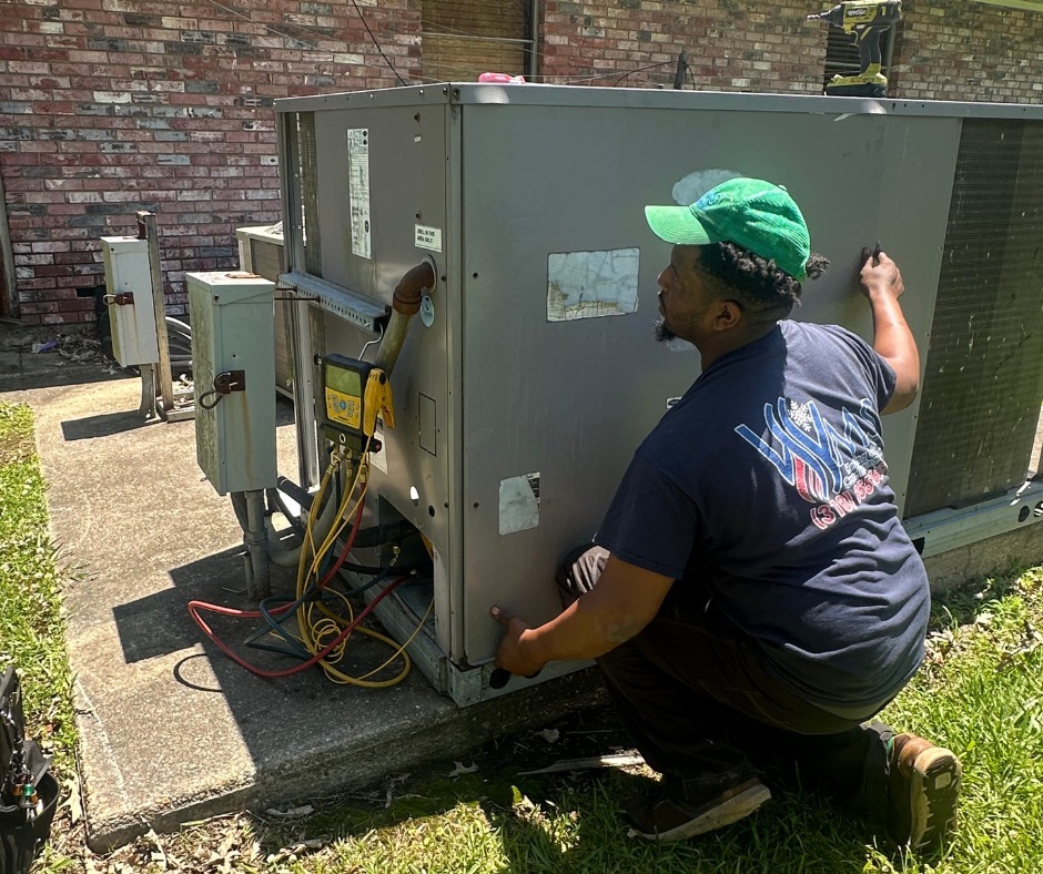 Technician inspecting an outdoor air conditioning unit, focusing on maintenance tasks. Green cap and work tools visible, emphasizing HVAC service context.