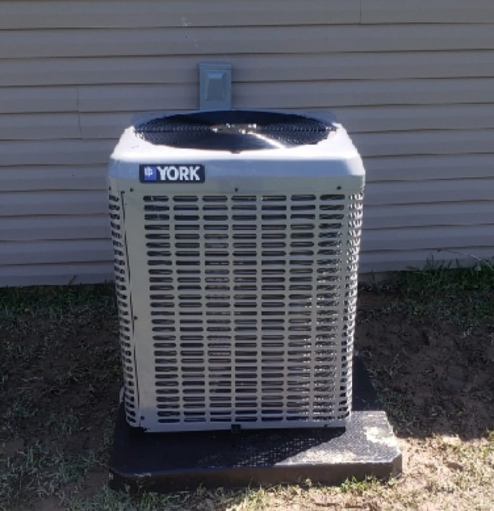 York air conditioning unit positioned outside a building on a concrete slab, showcasing its design and functionality for cooling purposes.